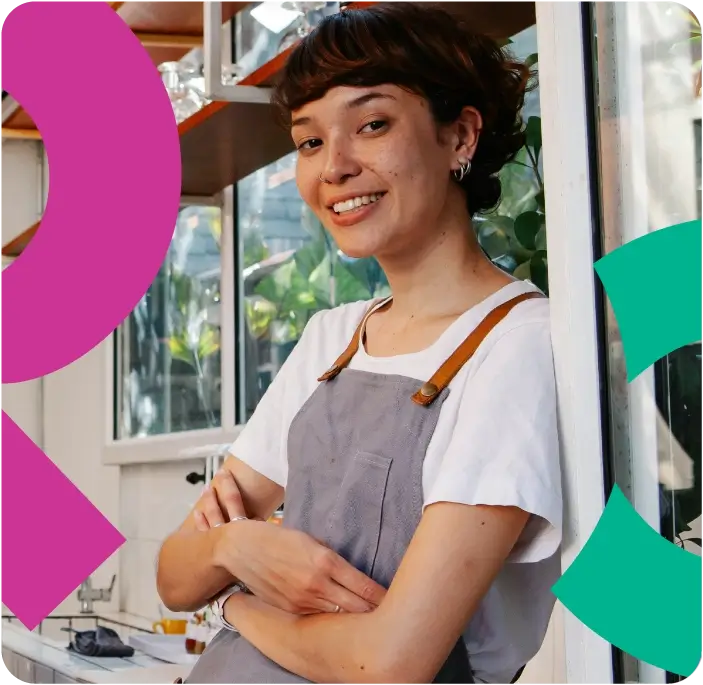 Woman in an apron leaning against a wall smiling