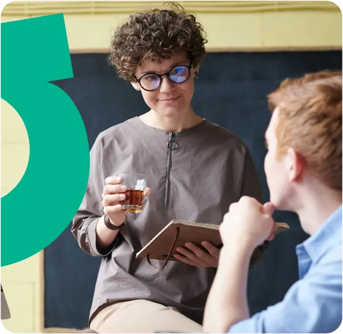 Two people chatting, one holding a glass of whisky and holding a book